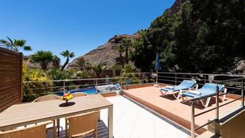 A rooftop pool area with lounge chairs, a table with fruit, and a view of a rocky hillside.