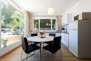 A modern kitchen with a round dining table, black chairs, a refrigerator, and a window with curtains.