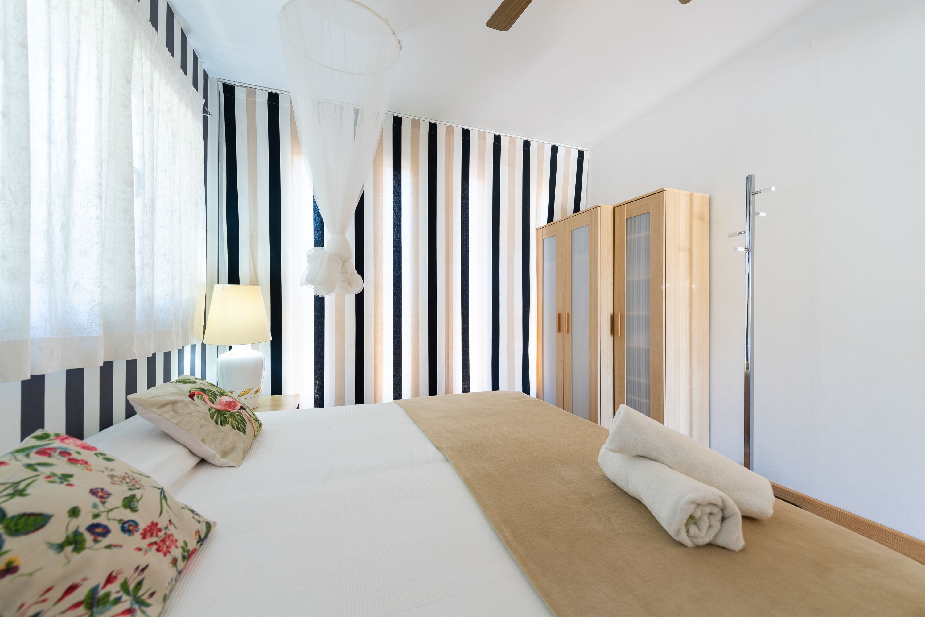 Une chambre d’hôtel comprenant un lit, une lampe de chevet, une fenêtre avec des rideaux, un miroir et une armoire en bois.