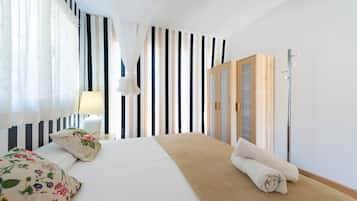 Une chambre d’hôtel comprenant un lit, une lampe de chevet, une fenêtre avec des rideaux, un miroir et une armoire en bois.