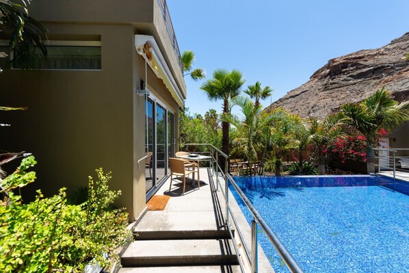 A swimming pool with a clear blue water surface, surrounded by palm trees and a building with a balcony.