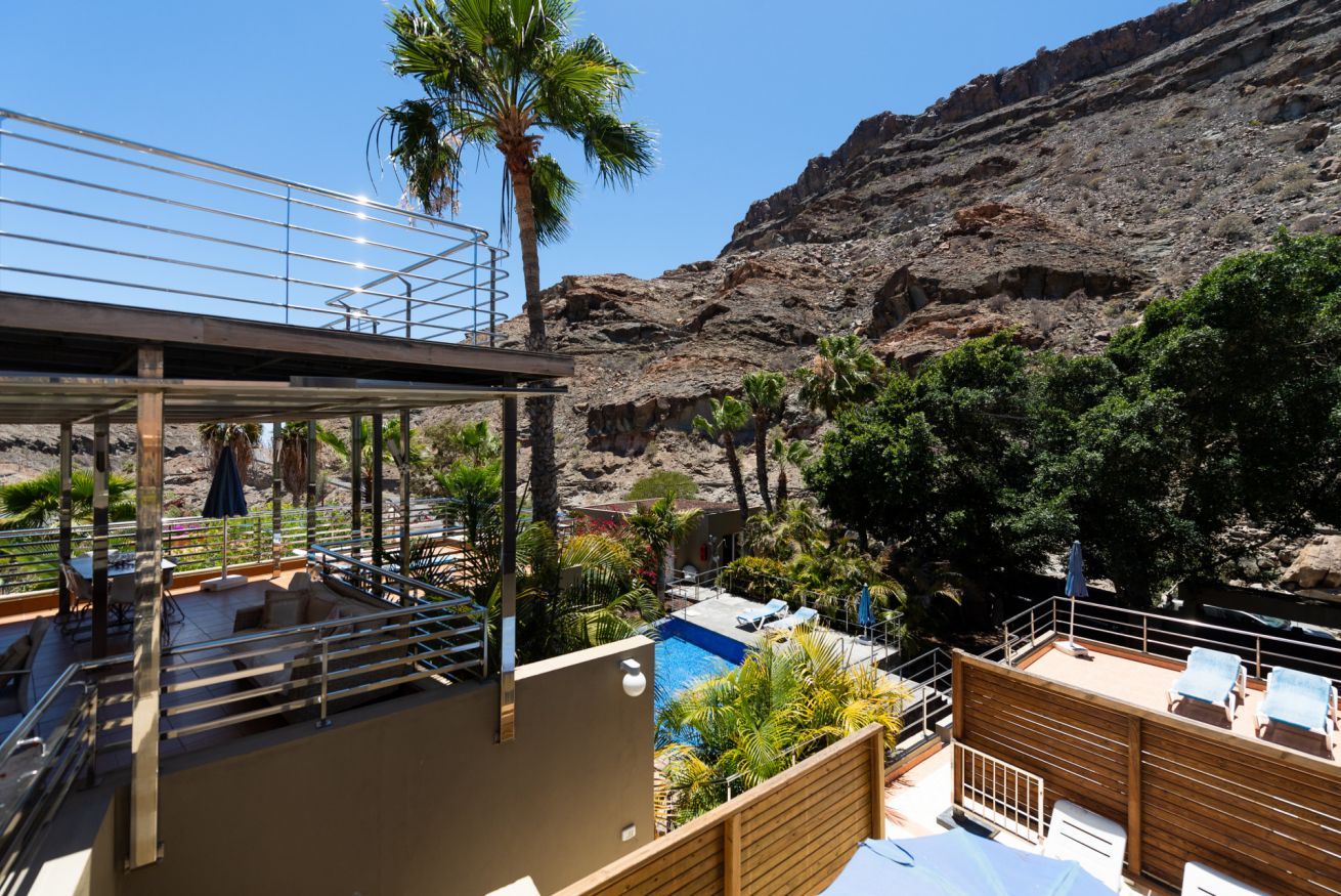 Un espace piscine aménagé sur le toit, avec des chaises longues et une vue sur une colline rocheuse.