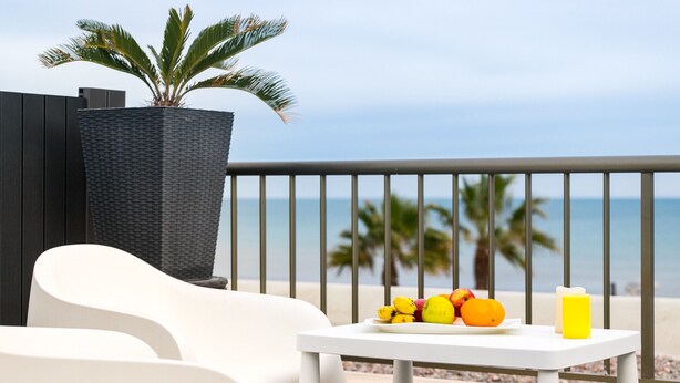 A balcony with a white table, a potted plant, and a view of the beach. - ApartUP Patacona Terrace Duplex II (Alboraya)