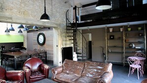 Een ruime loft met een hoge plafond, onbehandelde bakstenen muren, een trap en een eethoek met een klok aan de muur.