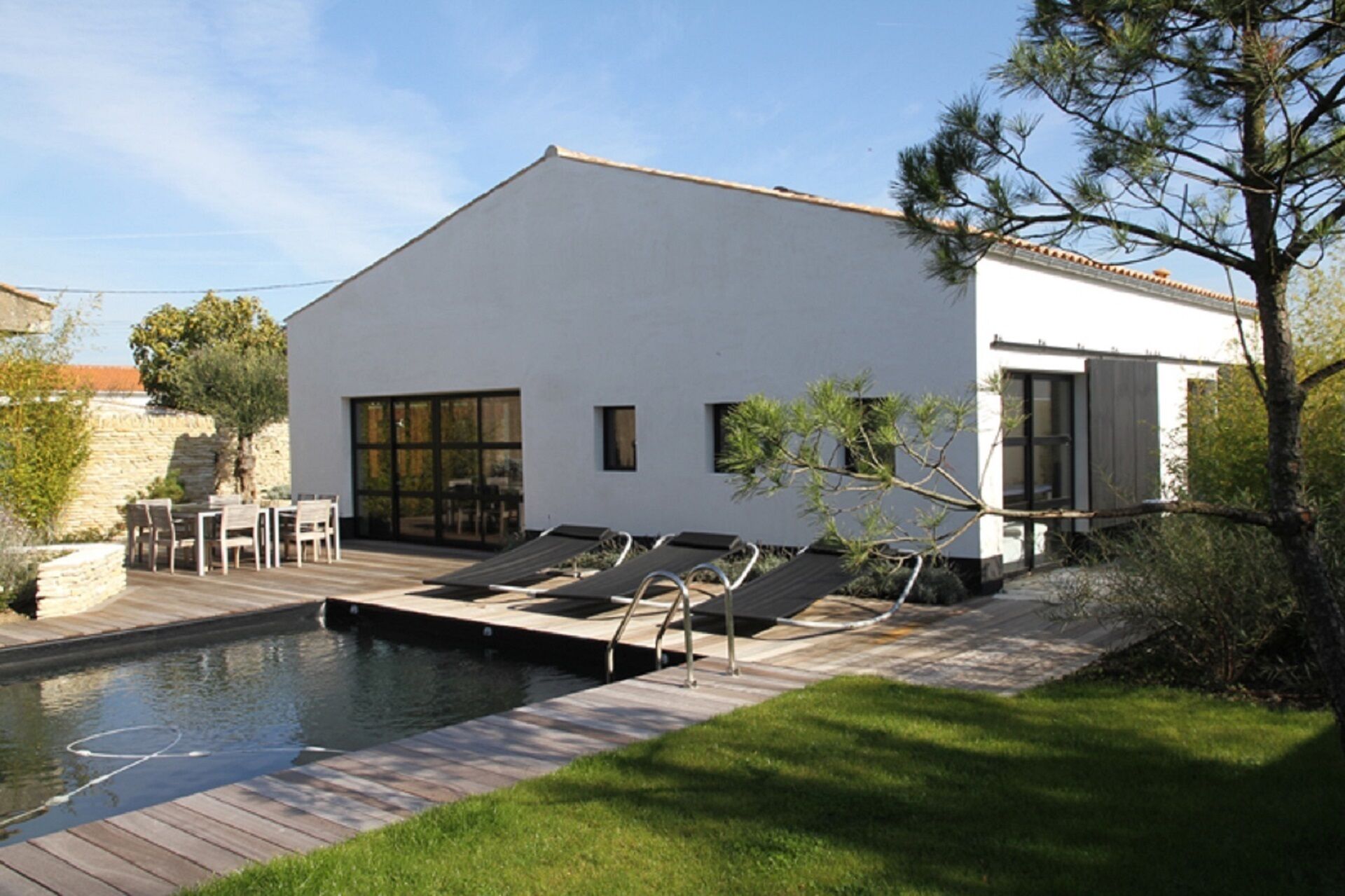 A modern house with a swimming pool, outdoor seating, and a stone wall.