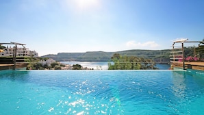 Piscina azul límpida com vista para um lago e colinas ao fundo.