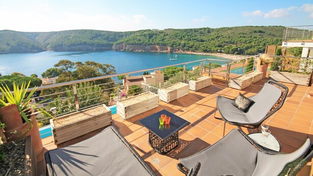 Terraço com área de estar ao ar livre, piscina e vista panorâmica da baía e colinas.