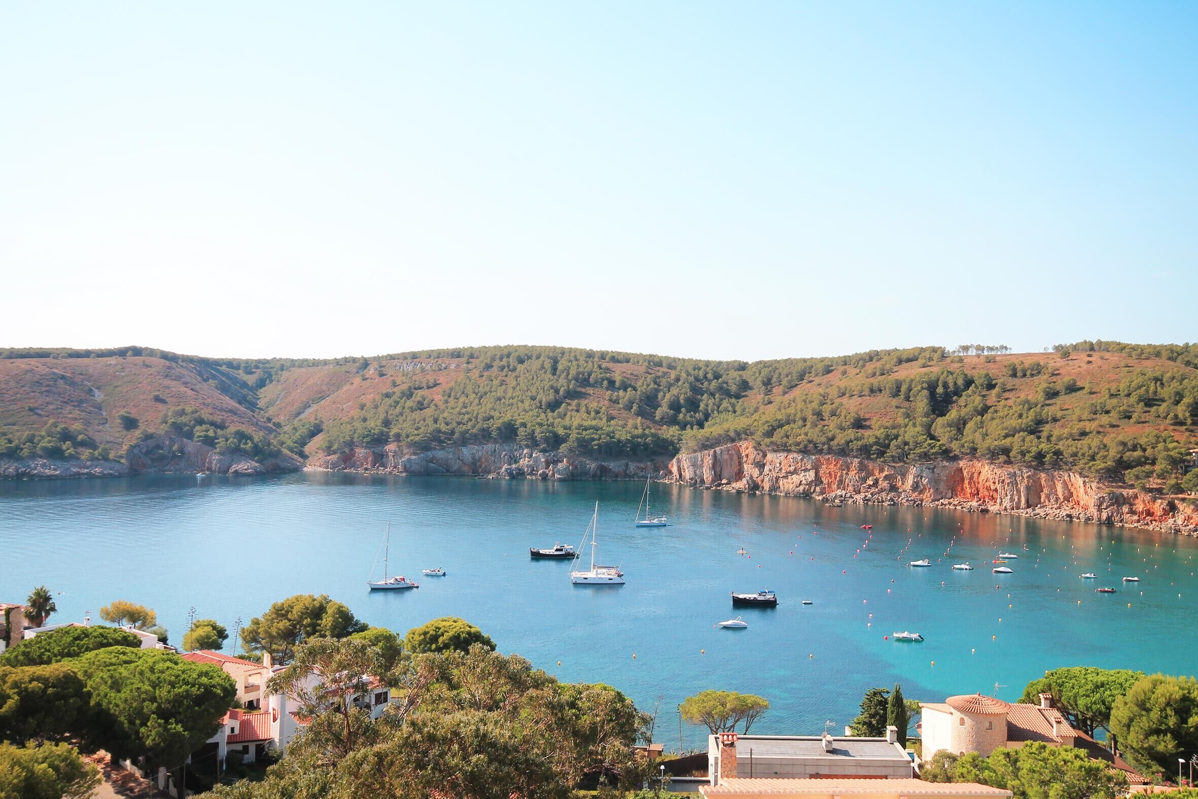 A coastal town with boats on a calm sea, surrounded by hills and greenery.