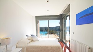Quarto com cama, mesa de cabeceira, luminária e vista para uma piscina e montanhas através de uma grande porta de vidro deslizante.