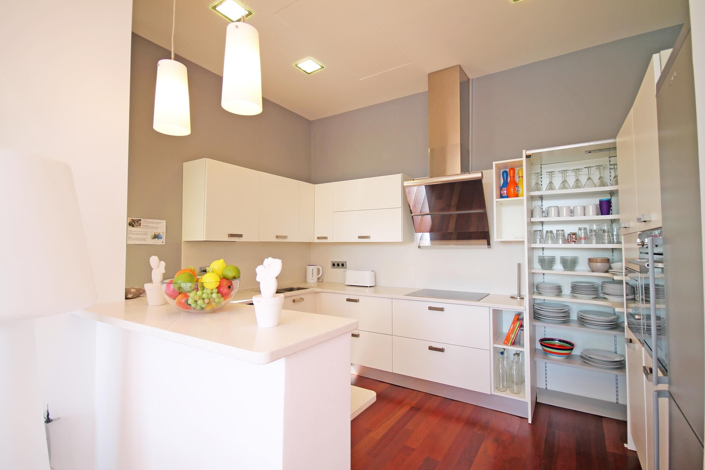 A modern kitchen with white cabinetry, a central island with fruit, and a built-in wine rack.