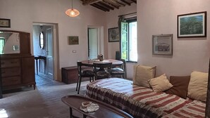A cozy room with a wooden ceiling, a round dining table, a sofa with striped bedding, and framed pictures on the walls. - VILLA OLIVI. (Nocchi)