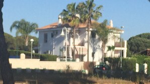 A white building with a red roof, surrounded by greenery and palm trees. - Semi-detached house in El Portil with private pool, free wifi, AC, BBQ  (El Portil)