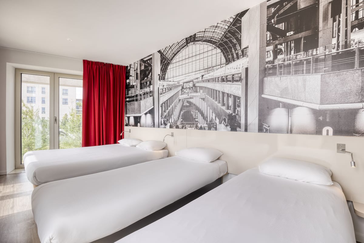 A hotel room with two beds, a large window, and a red curtain.