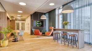 Moderni hotellin aula, jossa on puulattia, vastaanottotiski, baarijakkarat ja televisioruutu, jossa näkyy hotellin nimi.