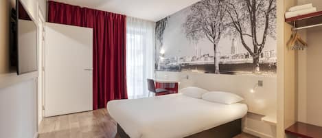 A modern hotel room with a large bed, a desk, and a cityscape mural on the wall.