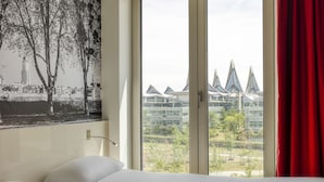 Hotellihuone, jossa on suuri ikkuna, sänky ja näkymä moderneihin rakennuksiin.