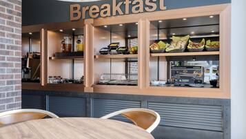 A breakfast counter with a sign, various food items, and a coffee machine.