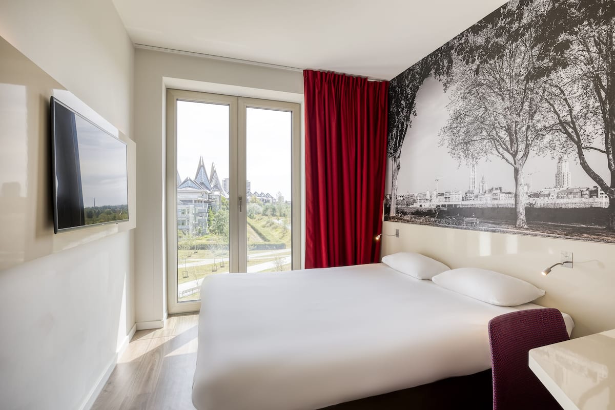 A hotel room with a bed, a TV, a red curtain, and a cityscape mural.