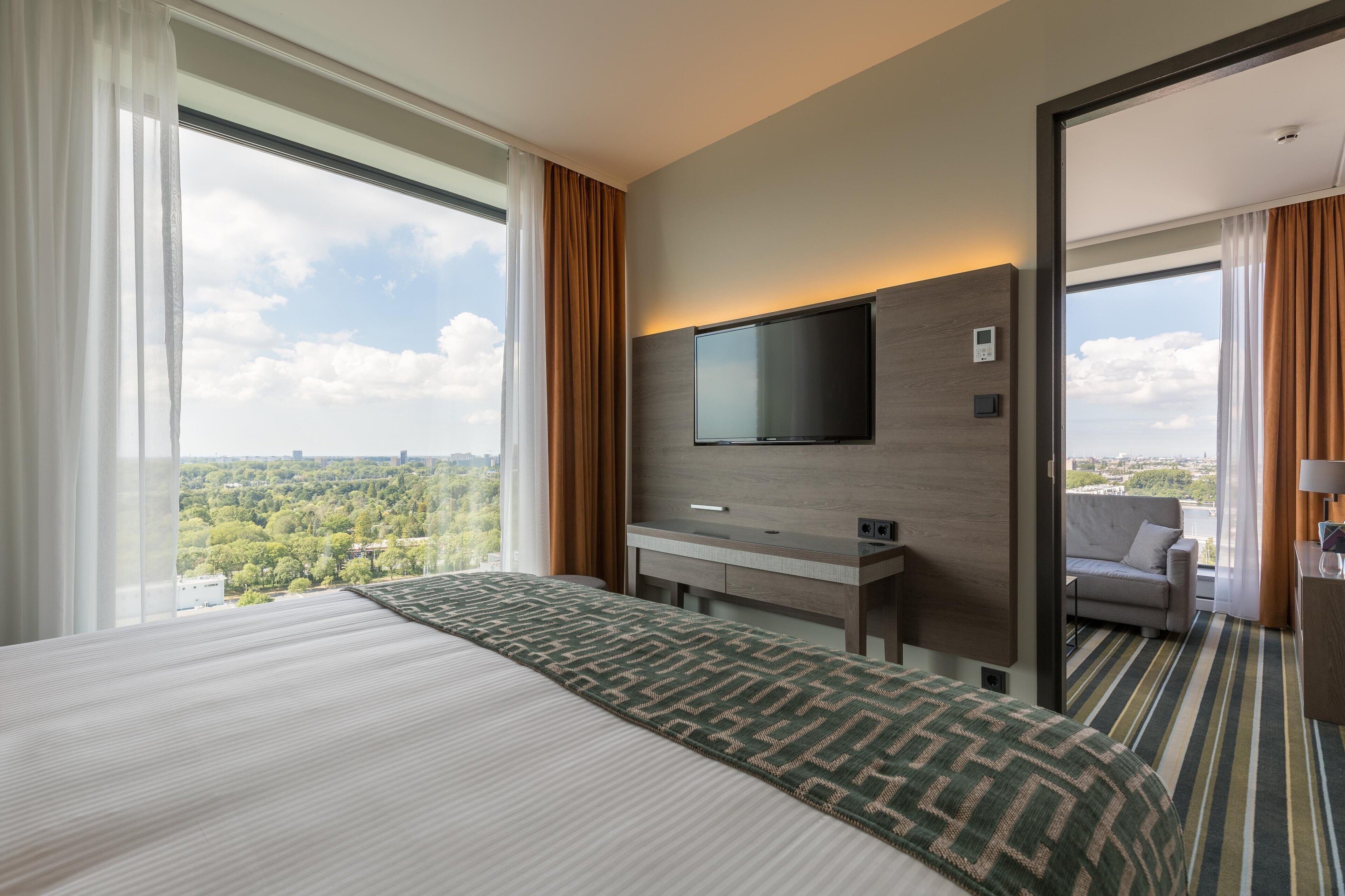 Hotelkamer met een groot bed, een aan de muur bevestigde televisie, een bureau en uitzicht op de stad.