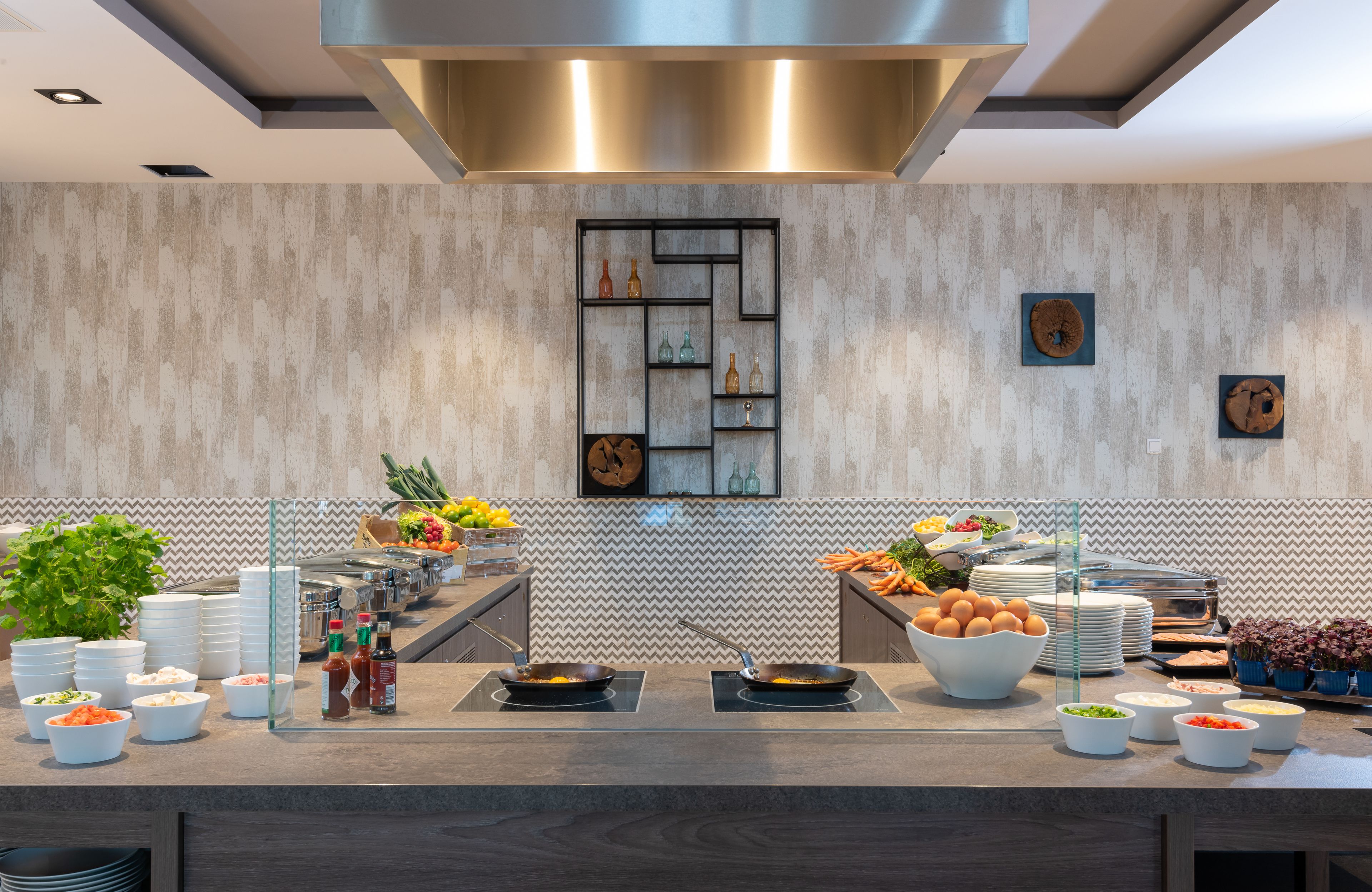 A modern kitchen with a central island, various food items, and a decorative wall with a geometric pattern.