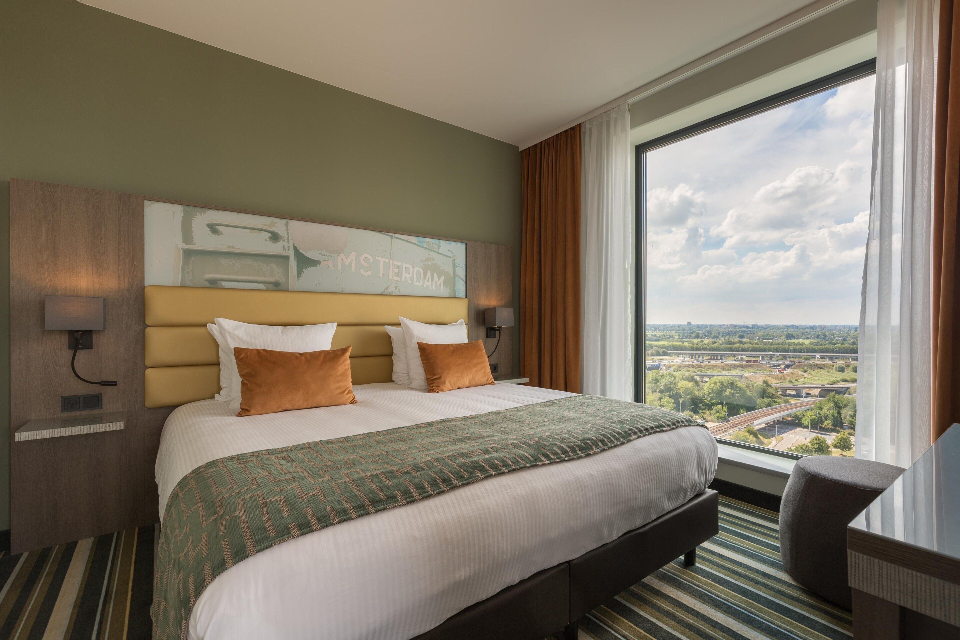 Habitación de hotel con una cama grande, vista a la ciudad y un cartel en la pared.