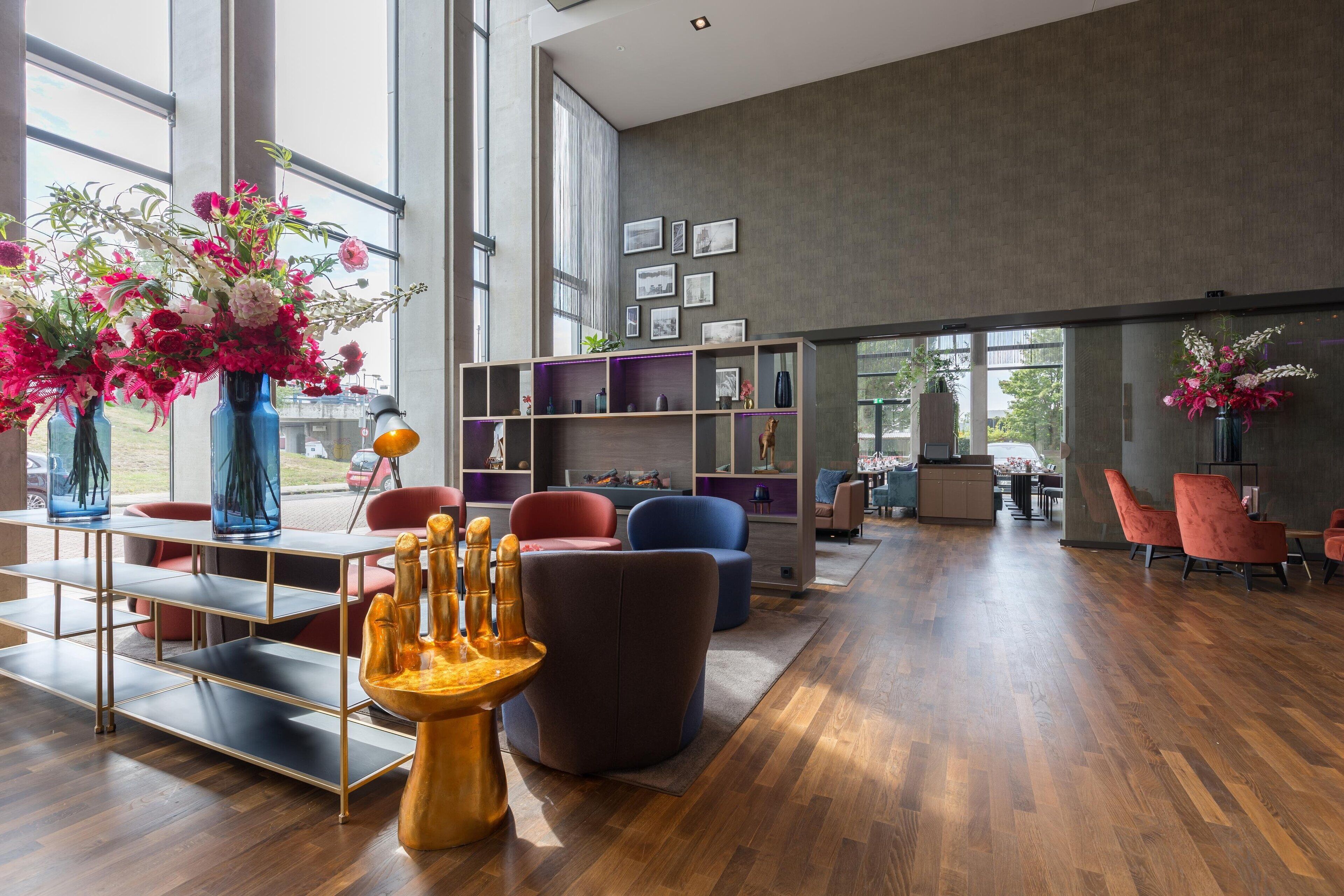 Amplia sala de estar con diseño moderno, que presenta piso de madera, un área de estar central con una mesa dorada y coloridos arreglos florales.