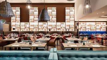 Un restaurant amb diverses taules i seients, una gran prestatgeria al fons i llums penjants.