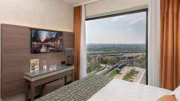 A hotel room with a bed, a desk, a TV, and a large window with a view of a bridge and highway.