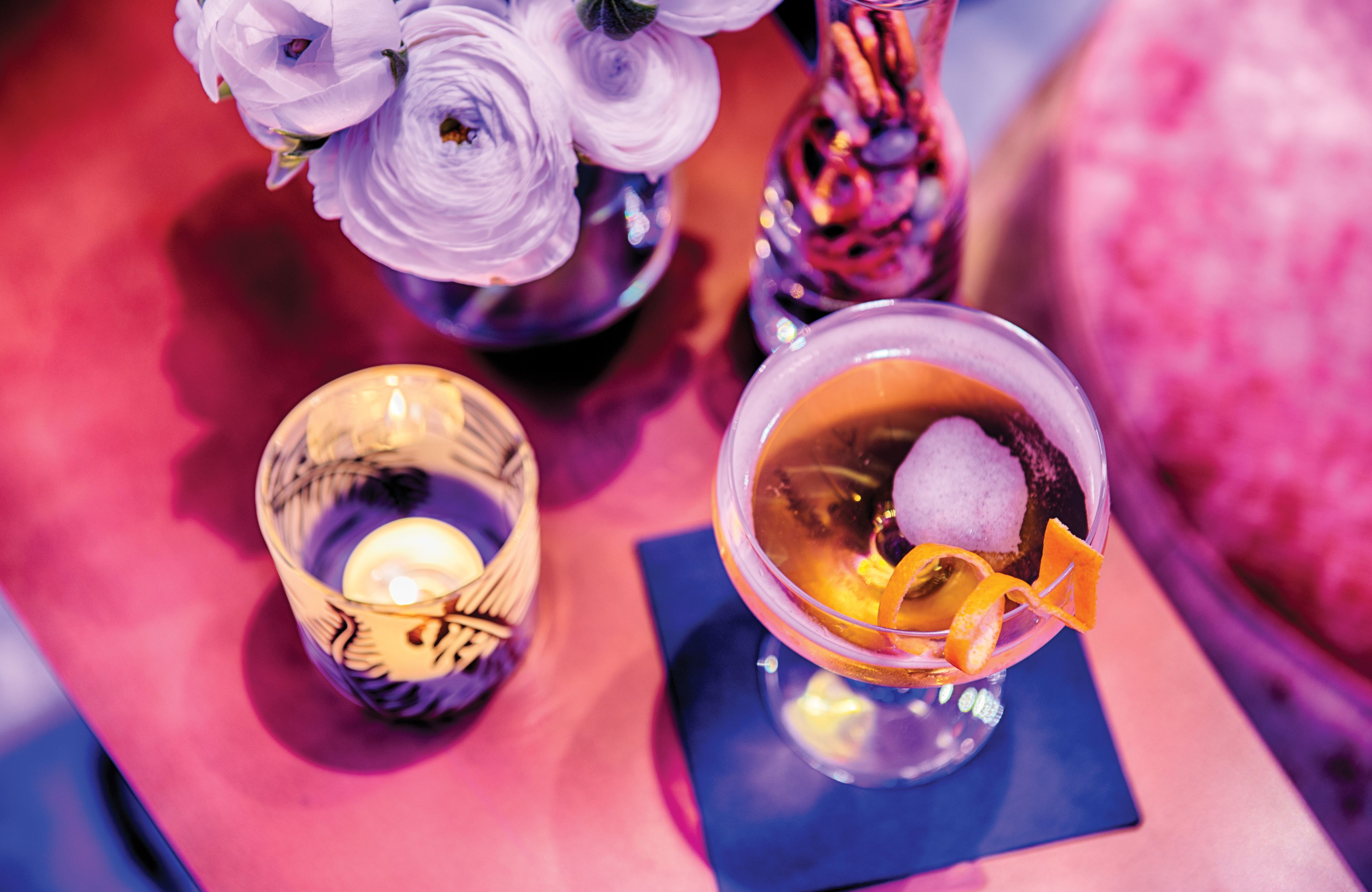 Una mesa con una vela, un vaso con una bebida y un florero con flores.