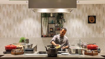 Un chef prépare un plat dans une cuisine moderne, équipée d’une grande cuisinière, de divers ustensiles de cuisine et d’un mur décoratif.