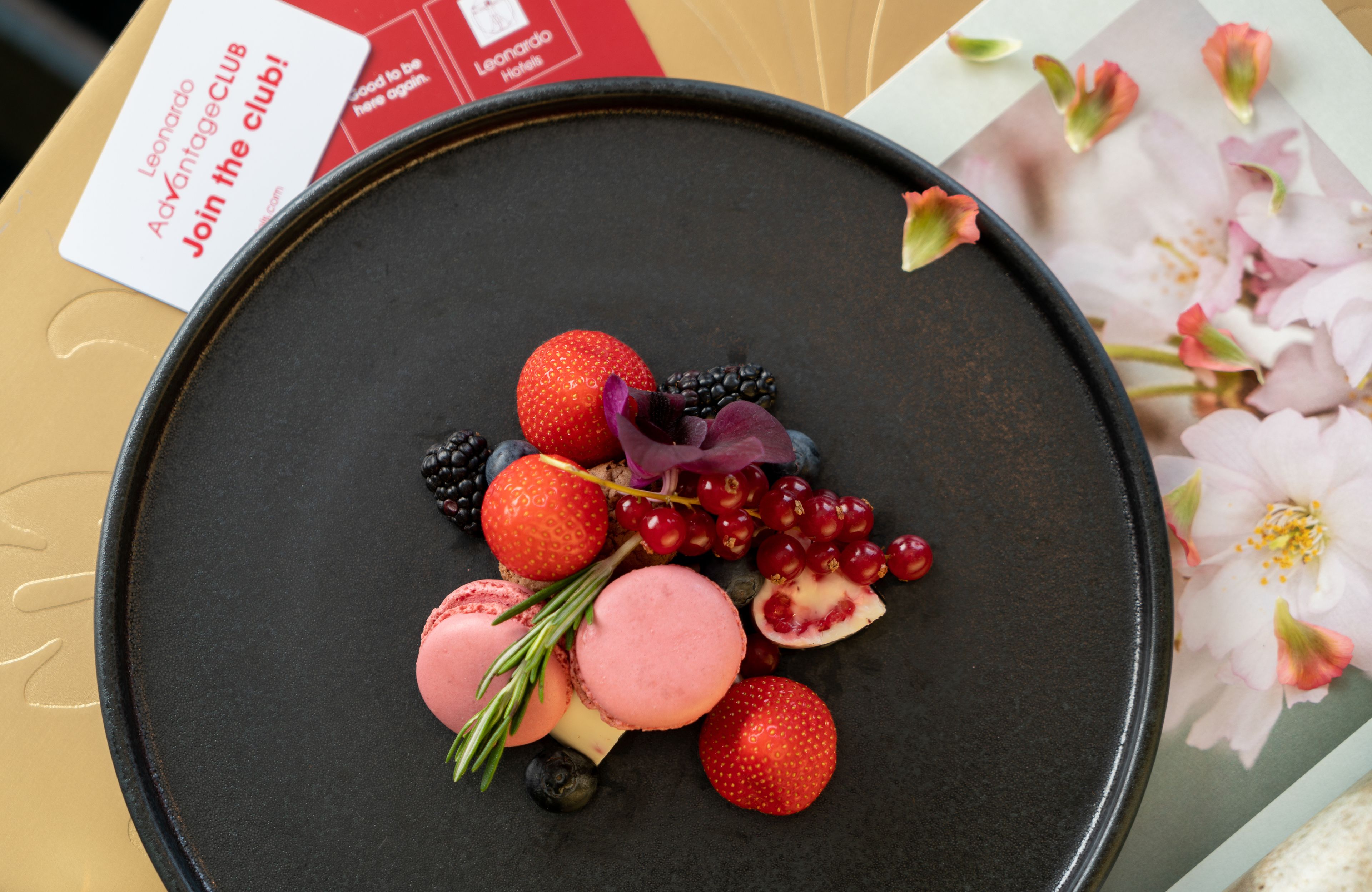 Eine Dessertplatte mit Erdbeeren, Brombeeren, Rote-Johannisbeeren und Macarons auf dunklem Untertisch.
