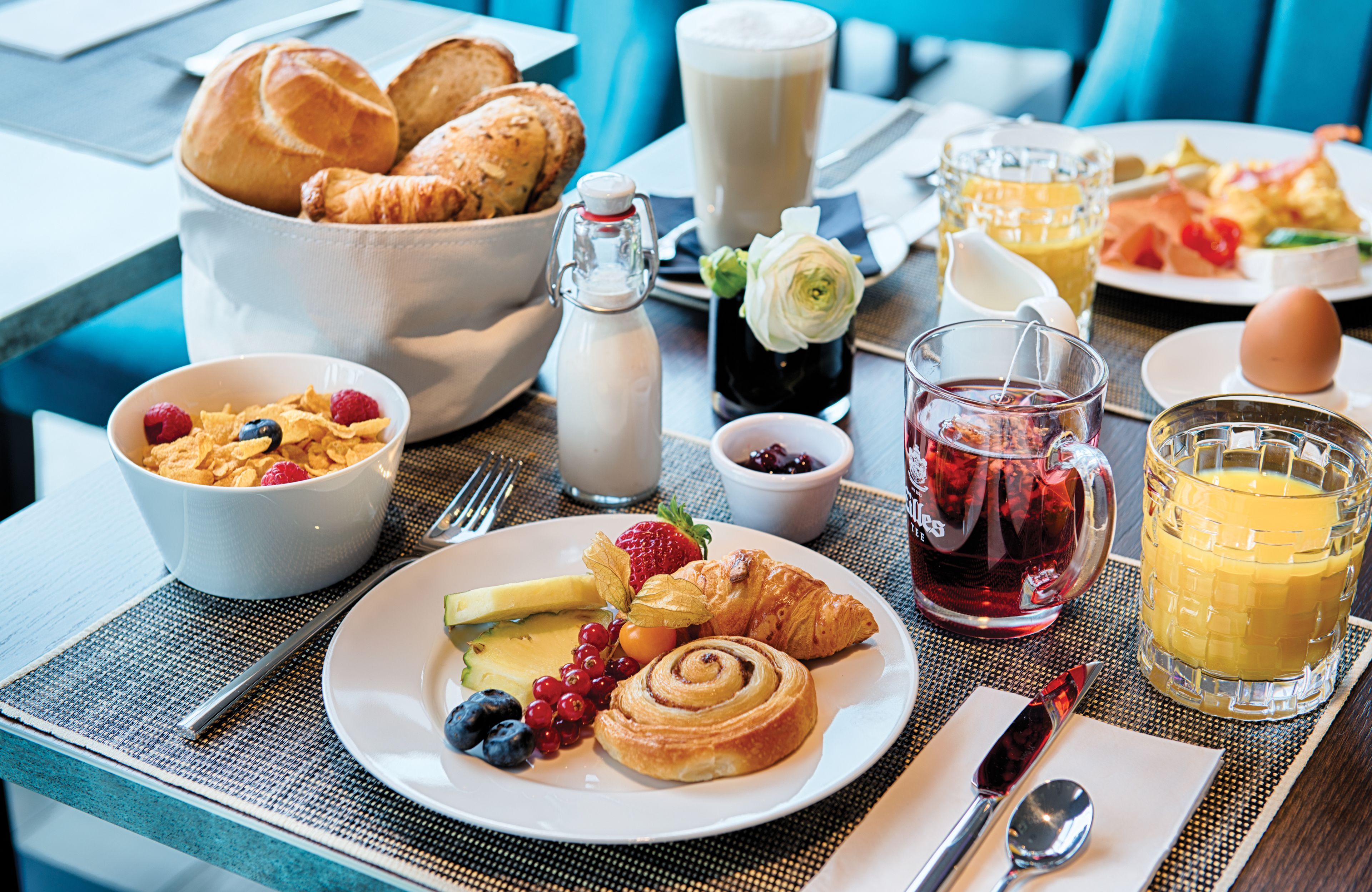 A breakfast setting with croissants, cereal, fruit, and beverages on a table.