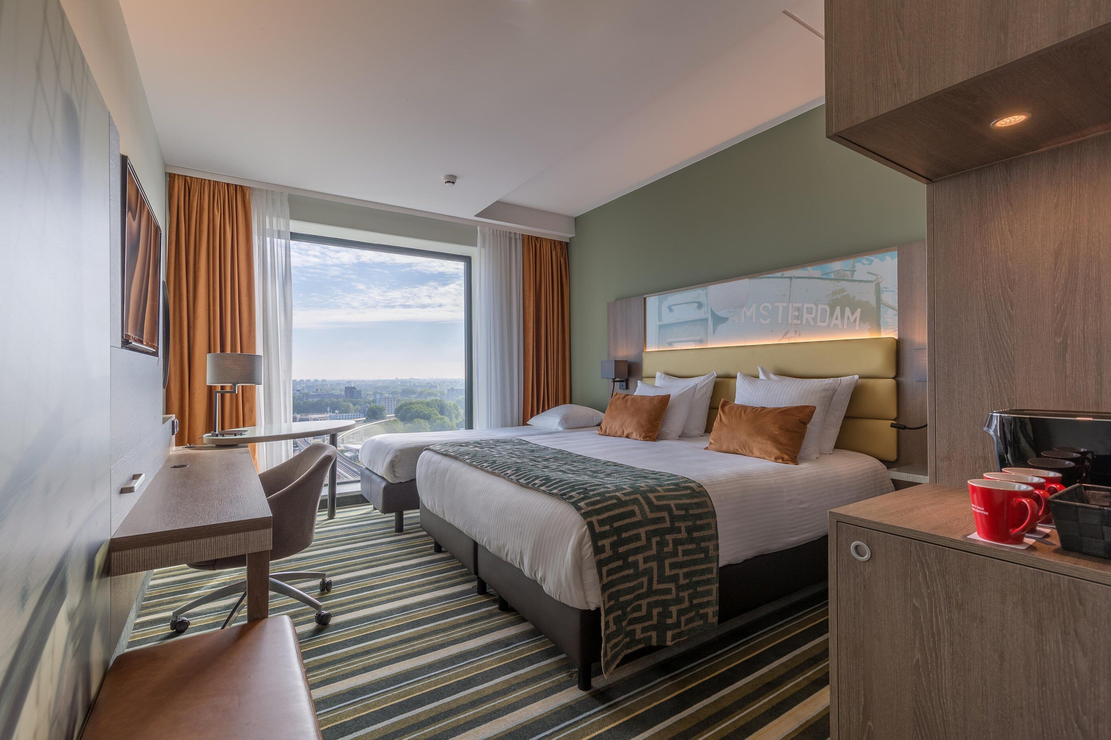 Una habitación de hotel con cama, escritorio, silla y vistas a la ciudad.