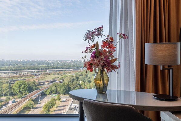 A hotel room with a view of a highway and greenery, a vase of flowers on a table, and a lamp. - Leonardo Royal Hotel Amsterdam (Amsterdam)
