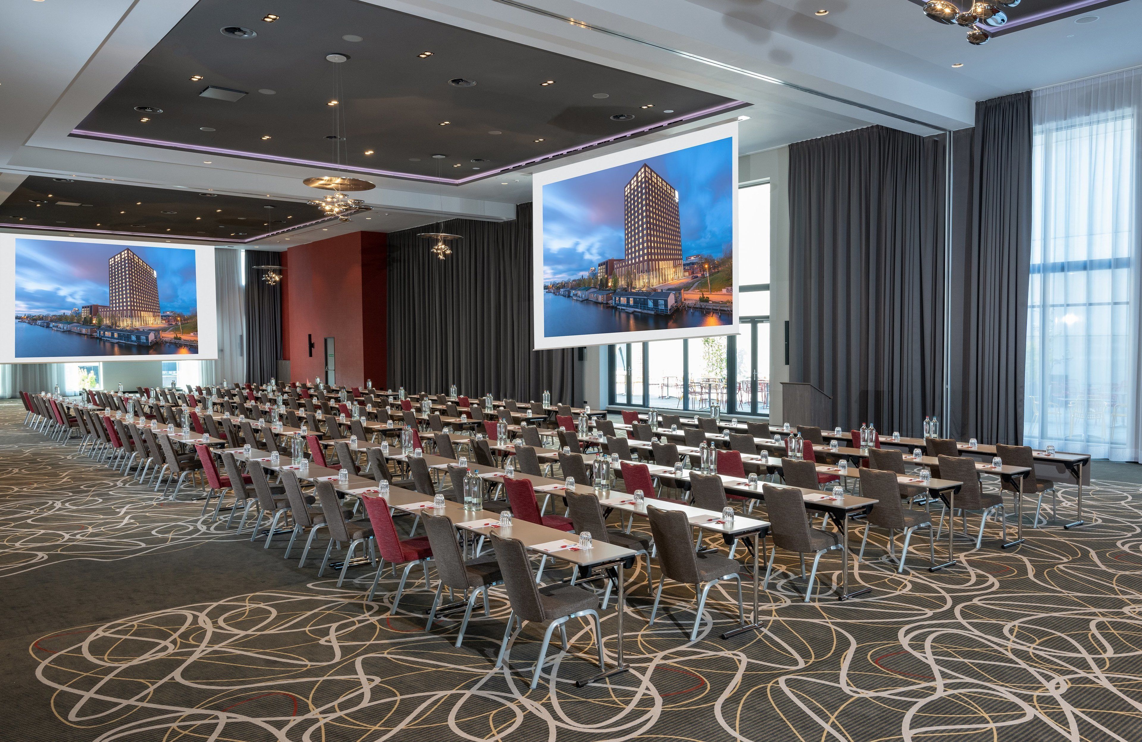 A conference room with rows of tables and chairs, large windows, and a modern ceiling design.