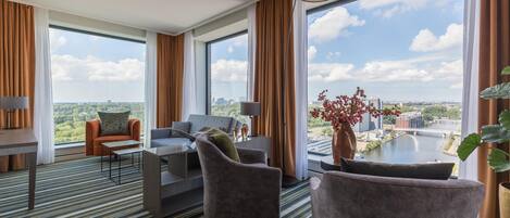 Habitación de hotel moderna con un amplio ventanal que ofrece vistas a la ciudad, alfombra a rayas y muebles contemporáneos.