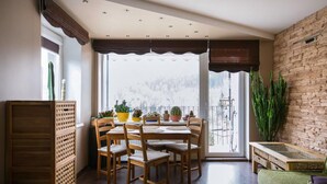 Un comedor con sillas y mesas de madera, un ventanal con cortinas y vista a un paisaje nevado.