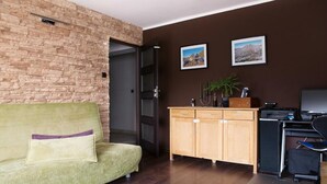 Una habitación con pared de ladrillo, sofá verde, mueble de madera y escritorio con computadora.