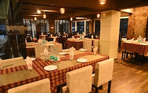 A restaurant with multiple tables set for dining, each with a tablecloth and chairs. - Alhind Calicut Tower (Kozhikode)