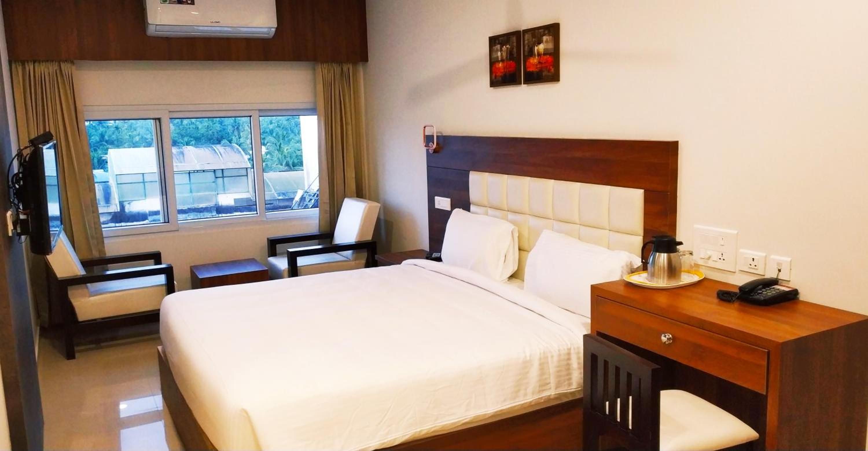 A hotel room with a bed, a desk with a telephone, a chair, and a window with curtains.