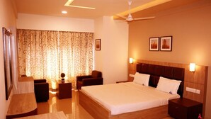 A hotel room with a large bed, a desk, a chair, a small table, and a ceiling fan. - Alhind Calicut Tower (Kozhikode)