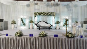 A stage with a white sofa, floral arrangements, and a backdrop with vertical drapes. - Alhind Calicut Tower (Kozhikode)