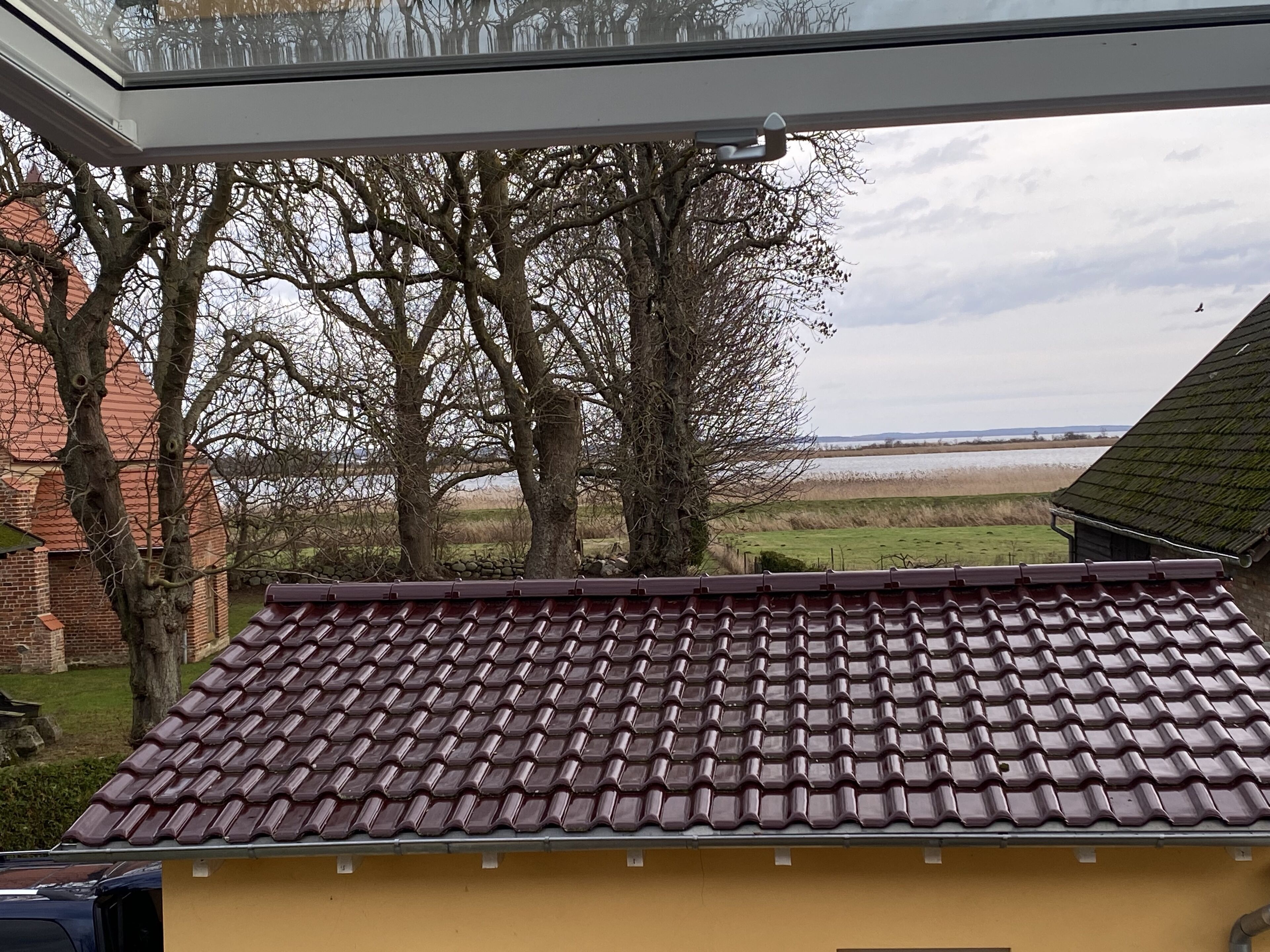 A yellow building with a red-tiled roof, surrounded by trees and a view of a body of water.