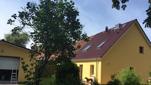 A yellow building with a red-tiled roof, a visible satellite dish, and a dog in the yard. - Ferienhaus Netzelkow am Achterwasser, Usedom, Baltic Sea, with WiFi, family-friendly (Lütow OT Netzelkow)