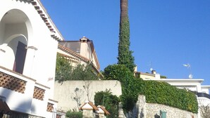 Una palmera alta frente a un edificio blanco con arcos y un muro de piedra.