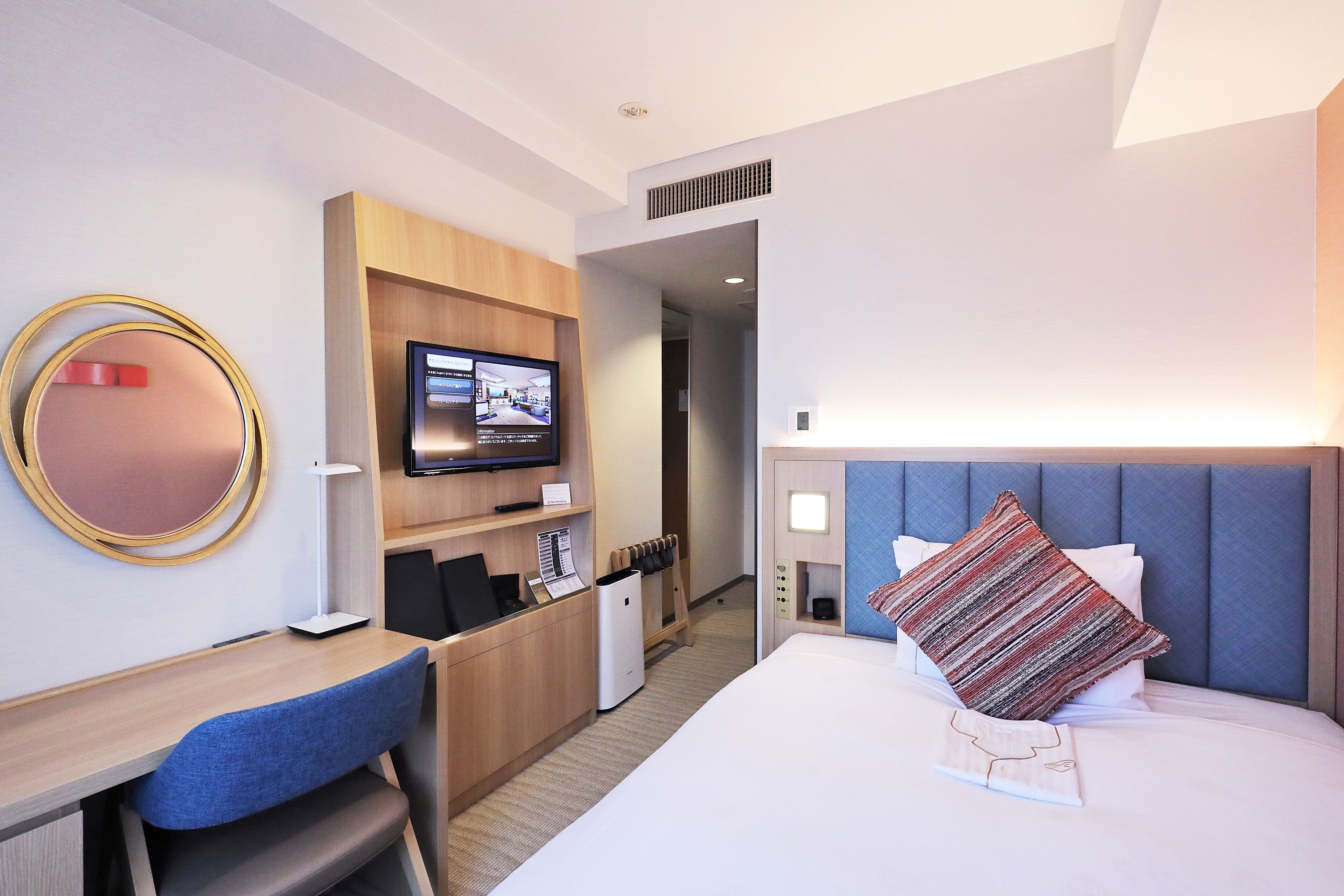 Habitación de hotel con cama, escritorio, silla, televisión y espejo.