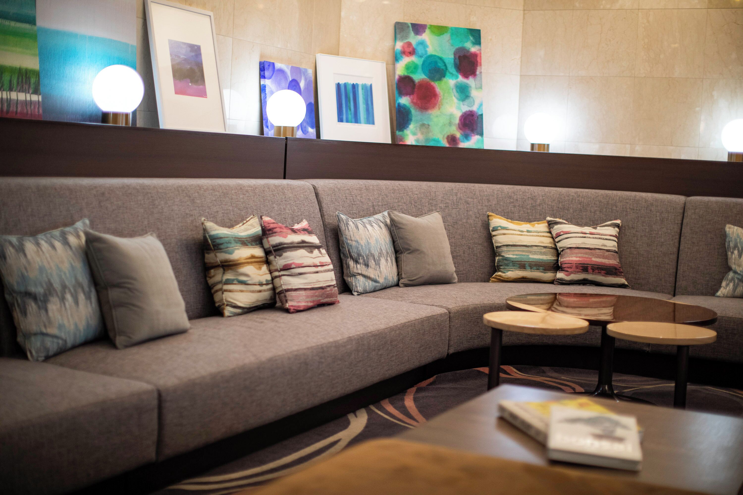 A modern lobby with a grey sofa, multiple pillows, a coffee table, and framed artwork on the wall.