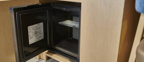 A compact refrigerator with a built-in freezer, situated in a wooden cabinet with a shelf above.
