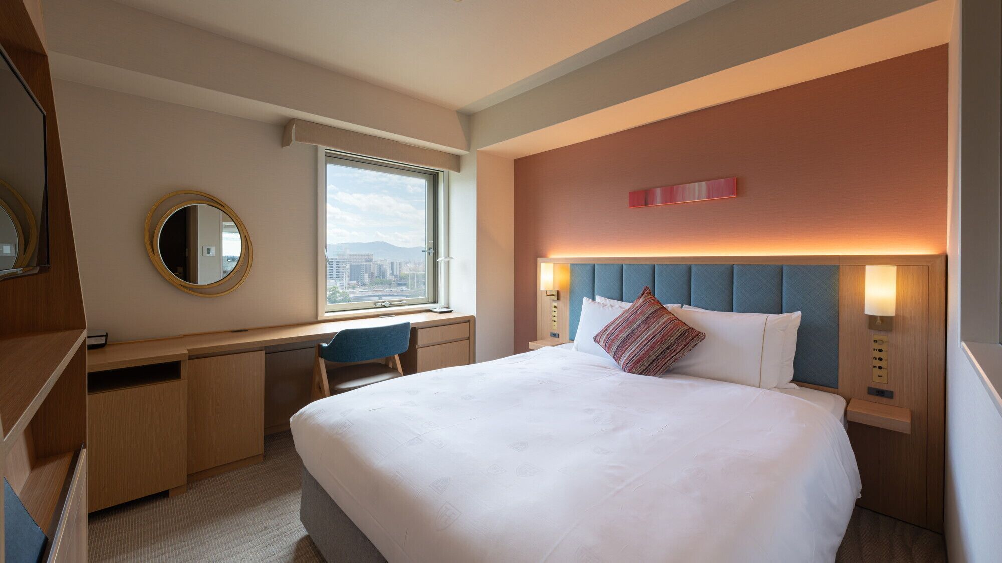 Habitación de hotel con cama, escritorio, silla y un ventanal con vistas a la ciudad.