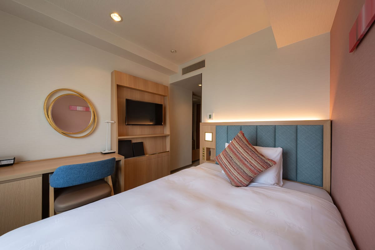 A hotel room with a bed, a desk, a chair, a television, and a mirror.